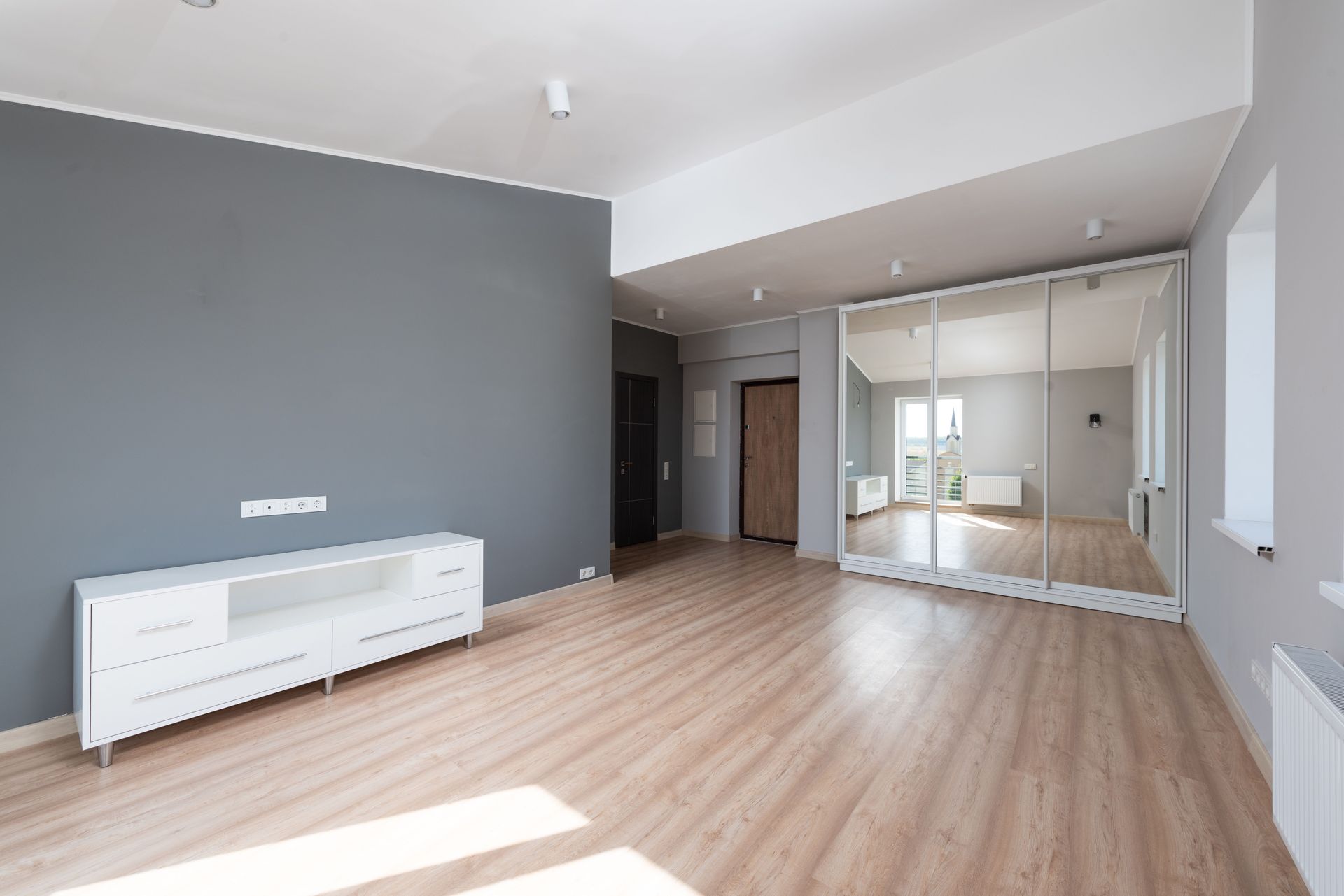Spacious empty room with wooden flooring and minimalist style furniture.