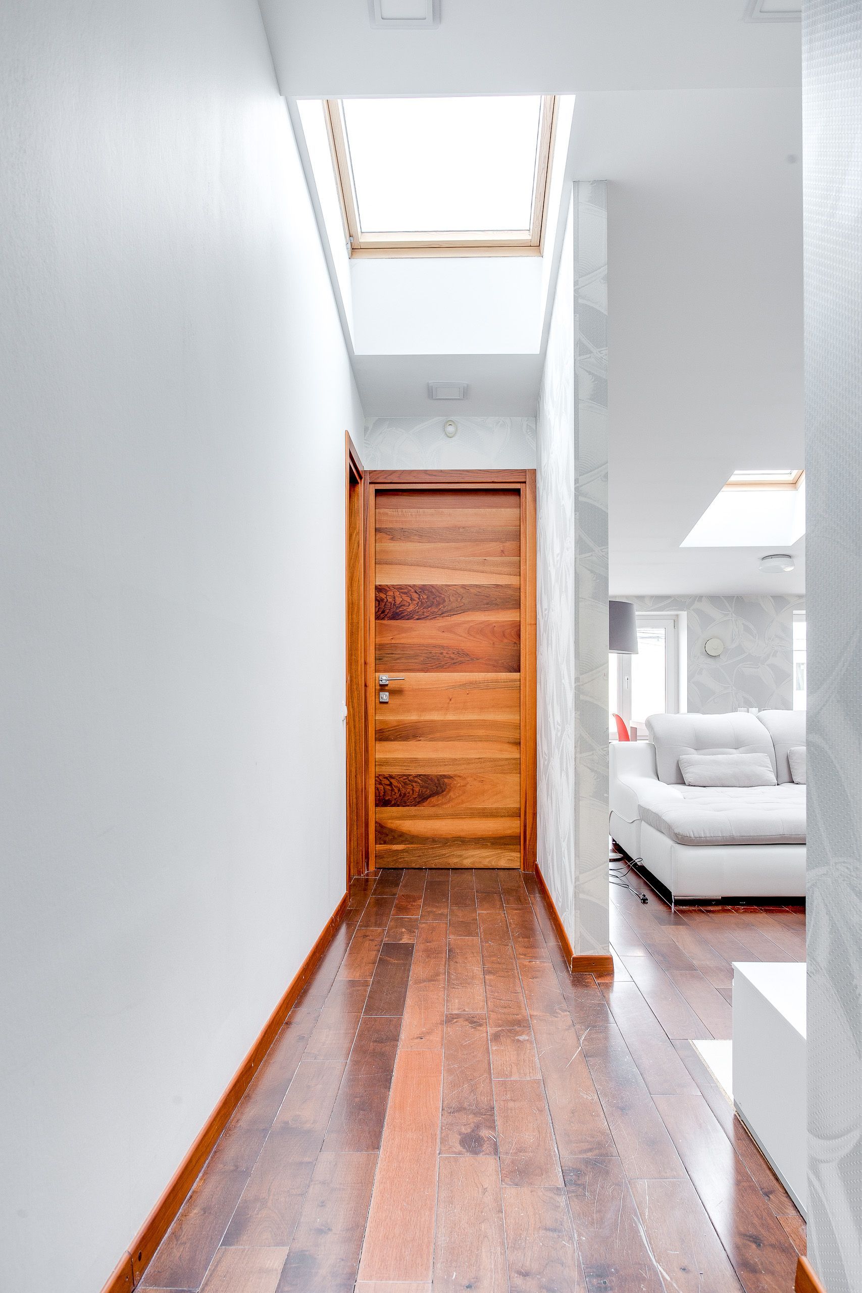 Minimalist corridor with wooden flooring and skylight, leading to a modern living area.